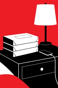 Three unopened cardboard book mailers stacked on a nightstand beside a lamp and a phone charging.