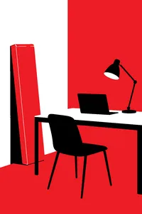 A long flat sealed box leaning against a wall behind a desk with a laptop, a desk lamp glowing beside it.