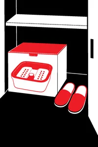 A boxed plastic foot bath on a closet floor next to a pair of worn slippers.